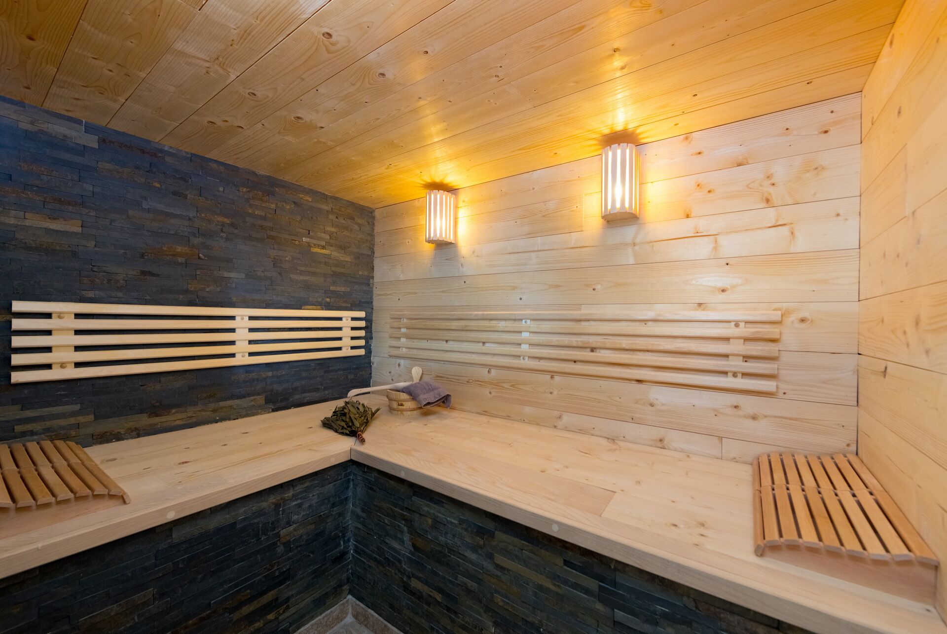 Una sauna con bancos de madera, paredes de piedra y dos luces fijadas a la pared.