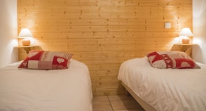 Duas camas de solteiro com roupa de cama branca e almofadas vermelhas estampadas, paredes de painel de madeira e luminárias de cabeceira.