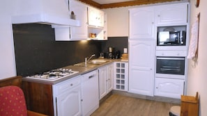 Uma cozinha compacta com armários brancos, fogão a gás, pia, micro-ondas e forno.
