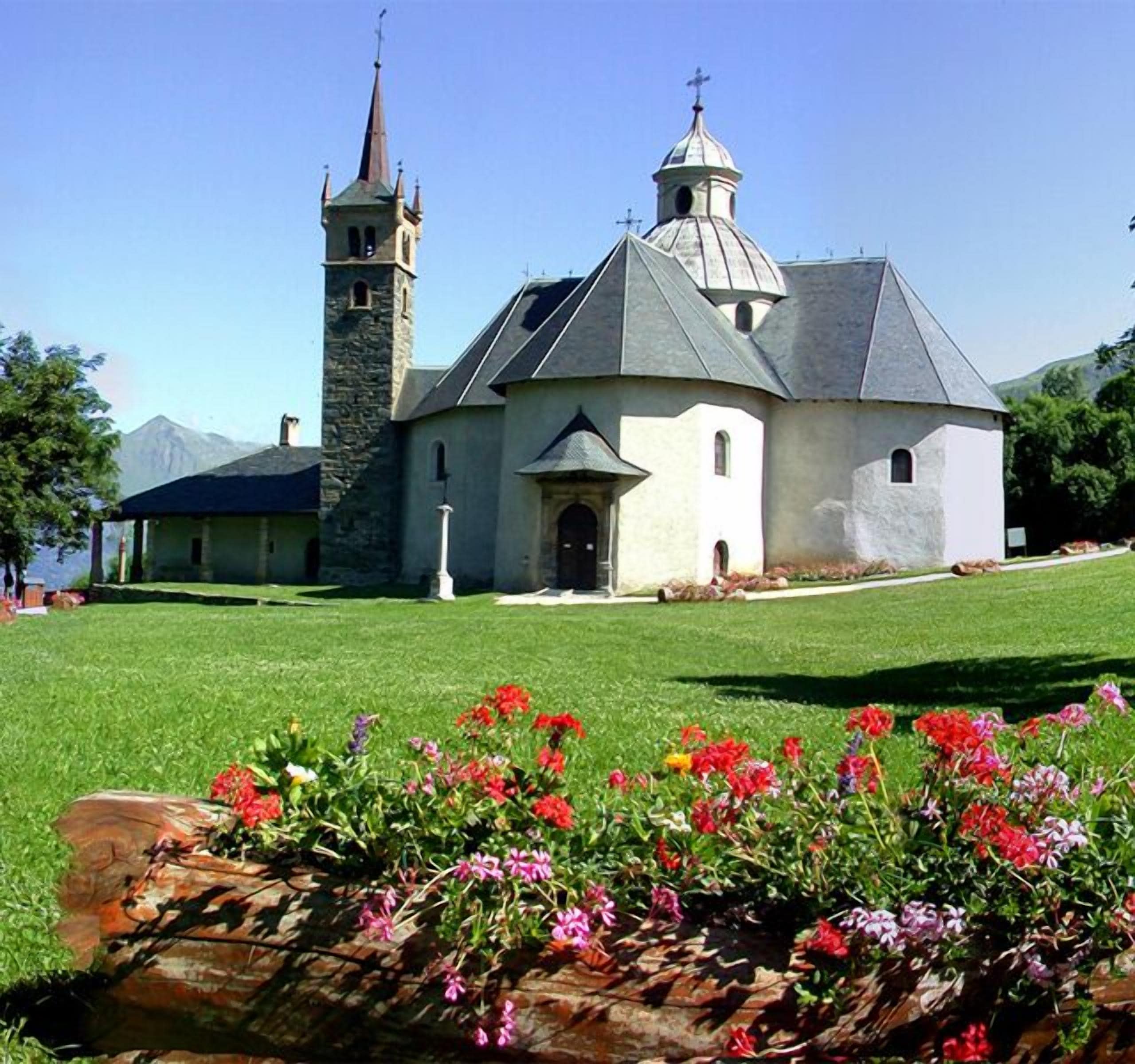 Una iglesia con un campanario y una cúpula, rodeada de un césped cuidado y flores de colores.