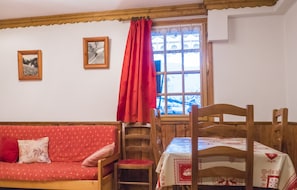 Um quarto acolhedor com uma mesa de madeira, um sofá vermelho e uma janela com vista para uma paisagem nevada.