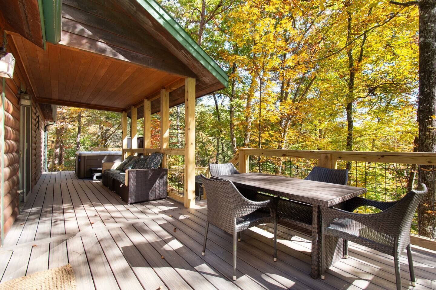 A wooden deck with outdoor furniture, including a sofa and chairs, overlooking a forest with autumn foliage.