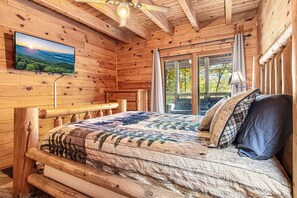 Een houten slaapkamer met een bed, een aan de muur bevestigde televisie en een raam met gordijnen.