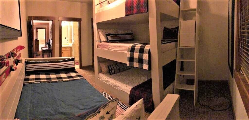 A dormitory room with bunk beds, a ladder, and a small desk.