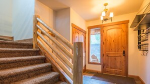 A wooden staircase with a handrail, a wooden door, and a chandelier. - Hawks Nest Townhome | 3 Bedroom | Mtn Views | Gas Grill | Gas Fireplace (Mt. Crested Butte)
