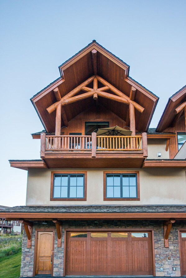 A two-story house with a wooden balcony, stone foundation, and a garage.