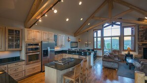 A spacious kitchen with wooden beams, a large island, and a view of the outdoors through large windows. - Hawks Nest Townhome | 3 Bedroom | Mtn Views | Gas Grill | Gas Fireplace (Mt. Crested Butte)