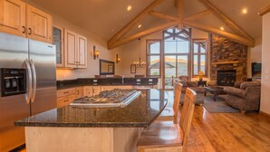 A spacious kitchen with a large island, wooden cabinets, and a stone fireplace. - Hawks Nest Townhome | 3 Bedroom | Mtn Views | Gas Grill | Gas Fireplace (Mt. Crested Butte)