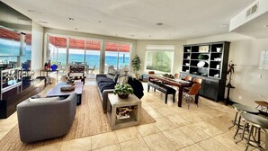 A spacious living room with a large window overlooking the ocean, a dining area with a view, and a kitchen with a built-in cabinet. - OCEANFRONT! 3 DISTINCT SUITES!
 JACUZZI & BBQ! (Encinitas)