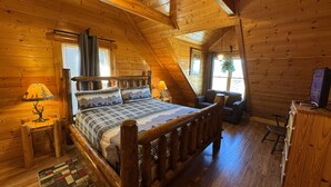 Une chambre confortable dans un chalet en rondins, avec un lit en bois, deux lampes de chevet, un petit bureau et un téléviseur.