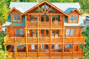 Ein mehrstöckiges Blockhaus mit Balkon, großen Fenstern und einer Veranda.