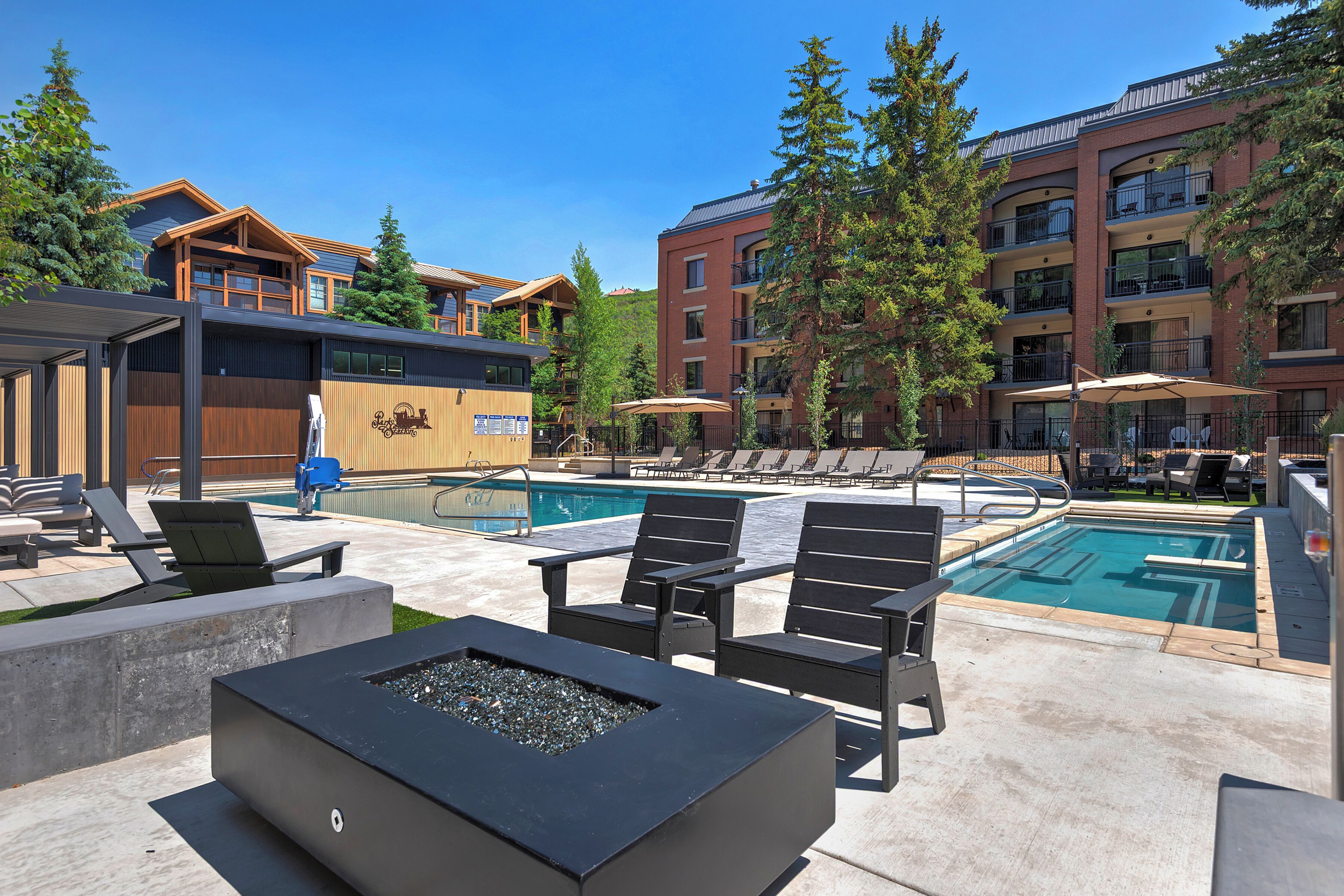 A pool area with lounge chairs, a fire pit, and a building with multiple balconies.