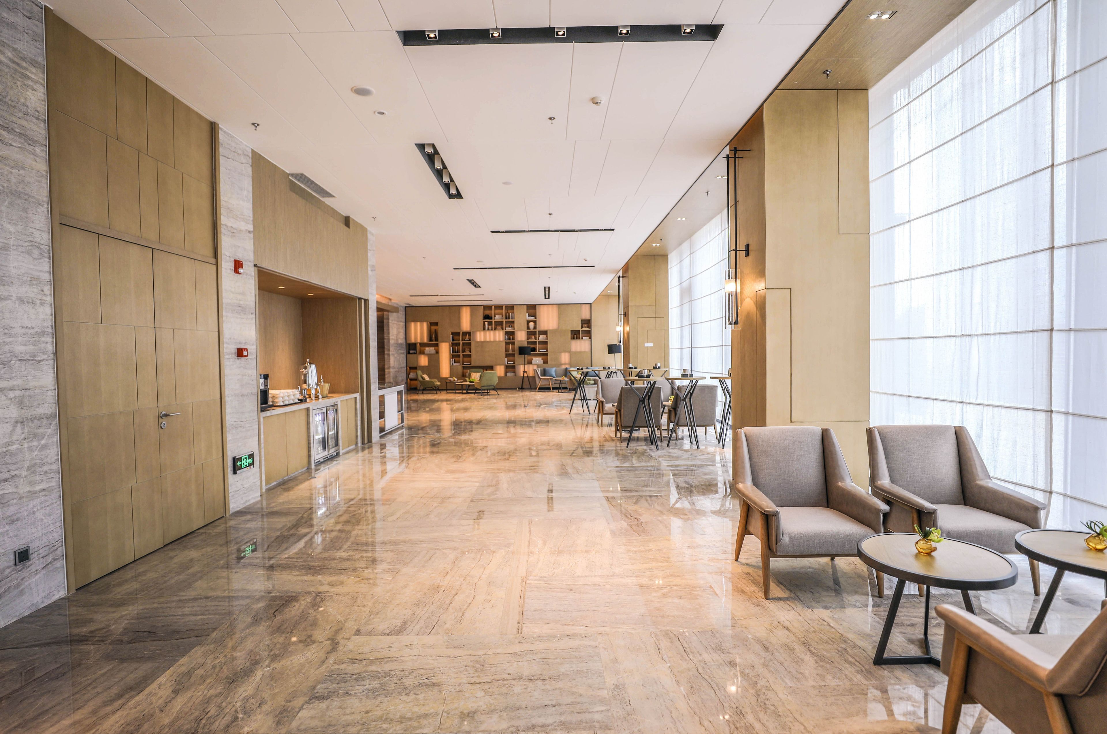 A spacious lobby with a polished marble floor, modern furniture, and large windows allowing natural light.