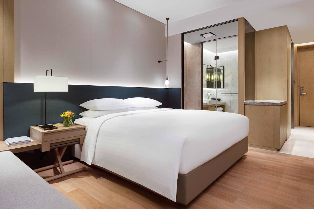 Een moderne hotelkamer met een bed, nachtkastje, lamp en een spiegel.