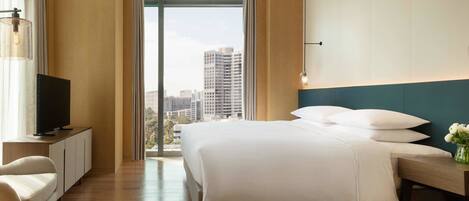 A modern hotel room with a large bed, a television on a cabinet, and a city view through the window.
