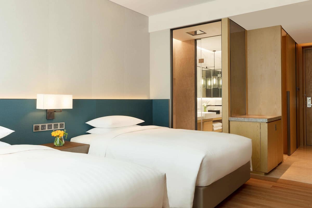 Een hotelkamer met twee bedden, een nachtkastje met een lamp, een bloemenvaas en een houten garderobe.