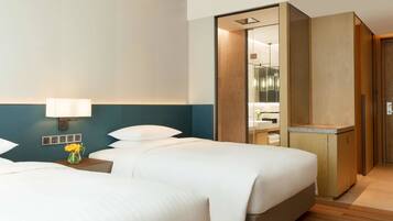 A hotel room with two beds, a nightstand with a lamp, a vase of flowers, and a wooden wardrobe.