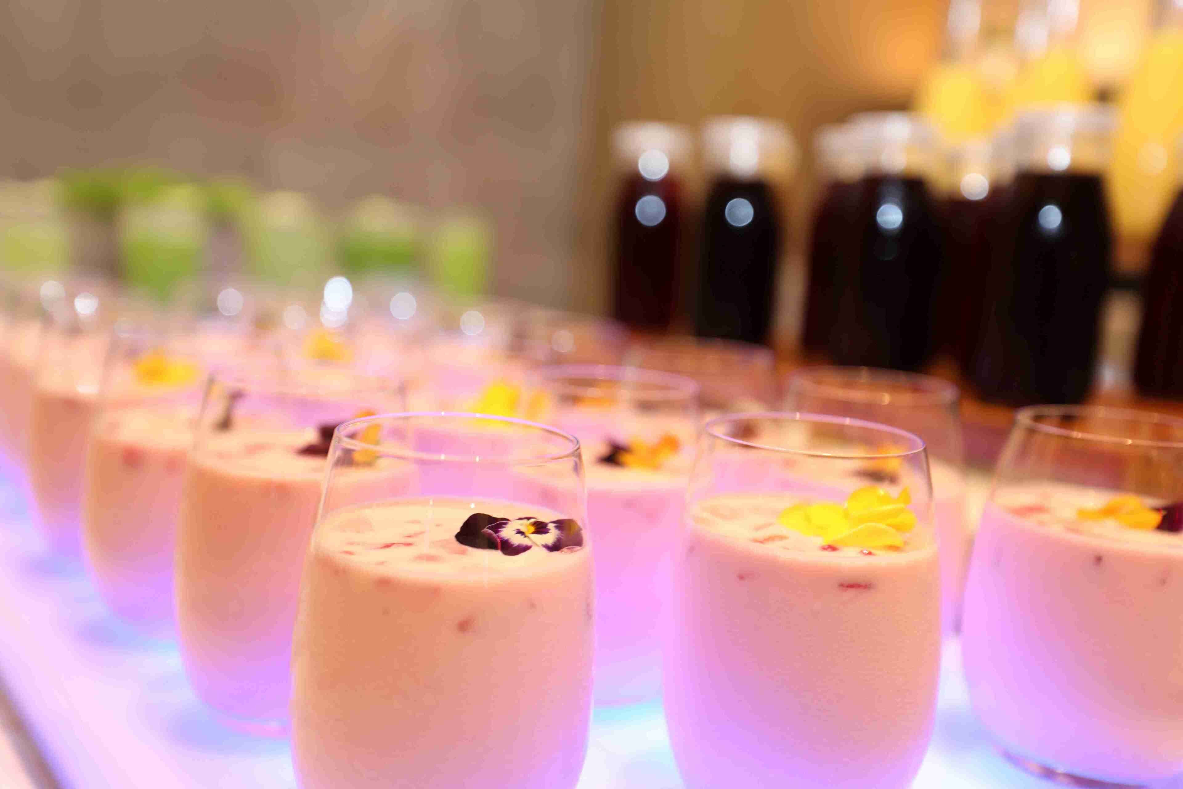 A row of glasses with a creamy beverage, garnished with edible flowers, on a bar counter.