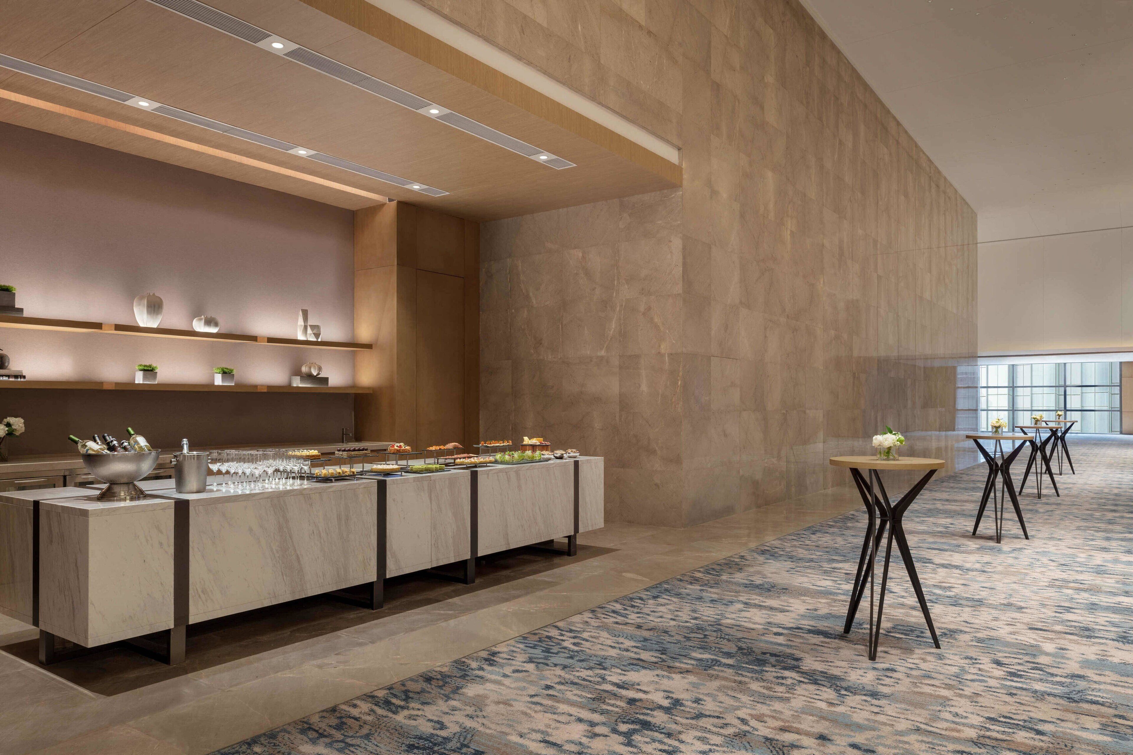 Un moderno vestíbulo de hotel con un mostrador de recepción de mármol, una zona de buffet y un suelo alfombrado.