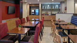 A modern restaurant with wooden tables and red upholstered booths. There is a TV mounted on the wall and a menu board in the background. - TownePlace Suites by Marriott Jackson (Jackson)