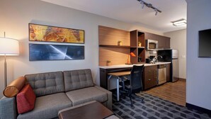A compact living space with a sofa, a small table, a kitchenette, and a patterned rug. - TownePlace Suites by Marriott Jackson (Jackson)