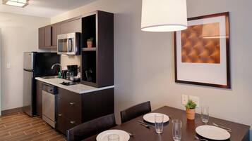 A compact kitchen with modern appliances, a dining table set for four, and a framed artwork on the wall.