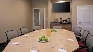Uma sala de conferência com uma mesa grande, cadeiras, uma TV presa à parede e um espaço para café.
