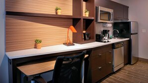 A modern kitchen with wooden cabinetry, a built-in microwave, a refrigerator, a coffee maker, and a small potted plant on the countertop. - TownePlace Suites by Marriott Jackson (Jackson)