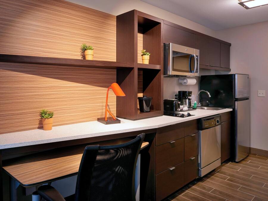 A modern kitchen with wooden cabinetry, a built-in microwave, a refrigerator, a coffee maker, and a small potted plant on the countertop.