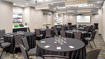 Un salón de conferencias con varias mesas redondas, cada una rodeada de sillas, equipado con tarjetas de identificación, bolígrafos y vasos.