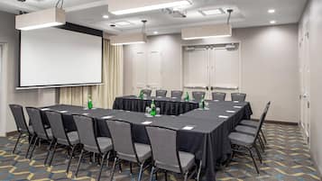 A conference room with a long table, chairs, a projector screen, and a carpeted floor.