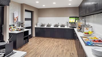 Une cuisine moderne dotée d’un îlot central, d’un comptoir-buffet proposant divers plats et d’un espace dédié au café.