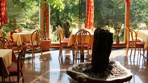 A restaurant with multiple tables and chairs, large windows with curtains, and a central decorative feature. - Waldhotel (Brilon)