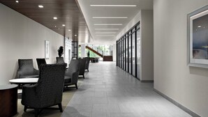A modern hallway with seating areas, a staircase, and large windows.