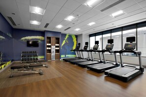 Ein Fitnessstudio mit Laufbändern, Hanteln und Bänken.