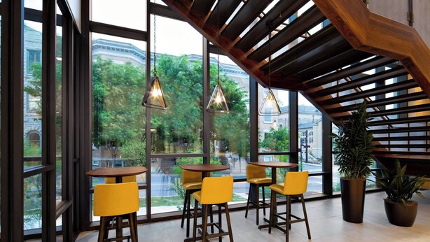 A modern interior with large windows, wooden ceiling beams, and yellow chairs.