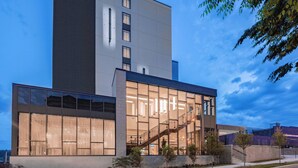 A modern building with a glass facade, a staircase leading to an upper level, and a landscaped area with trees.