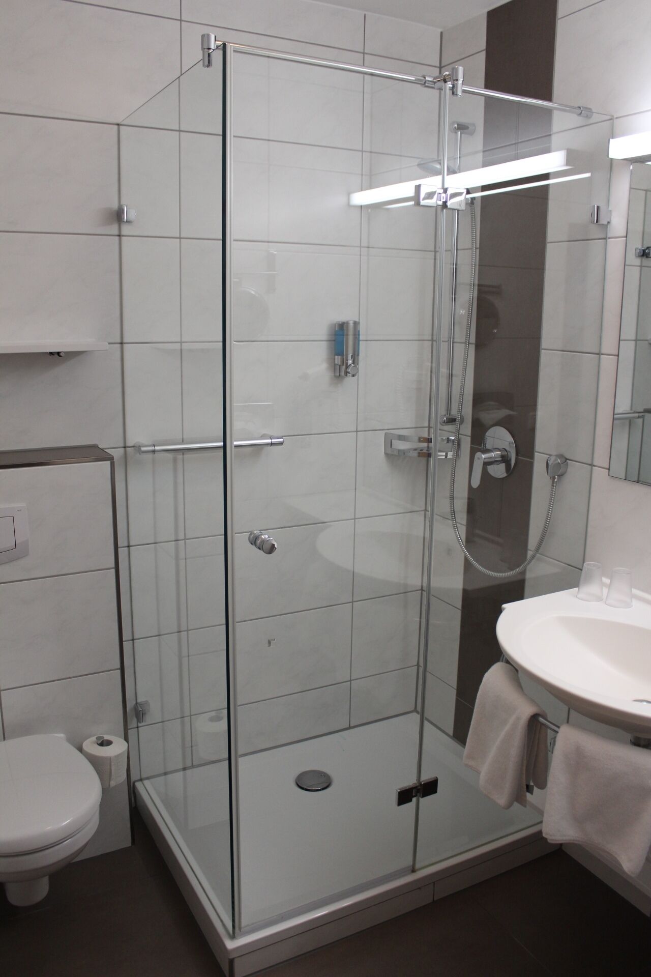 Een moderne badkamer met een douchecabine van glas, een wit wastafelmeubel en een toilet.