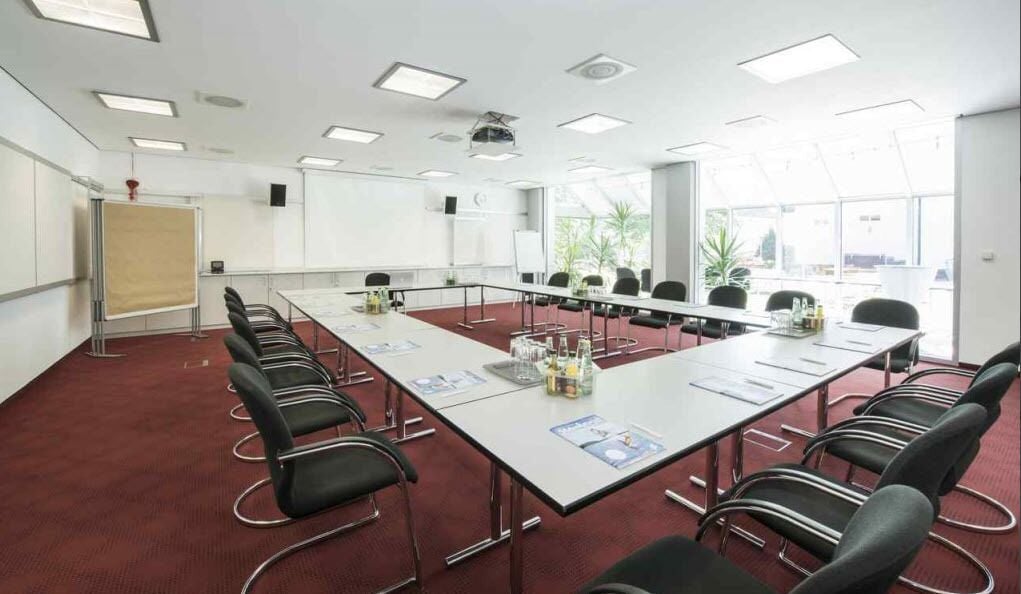 Una sala de conferencias con una larga mesa, sillas, un proyector y una pizarra.