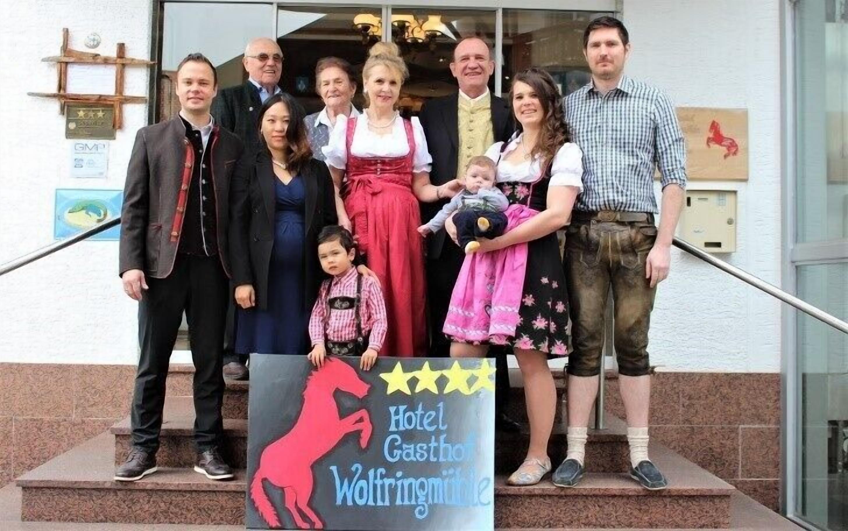 Een groep mensen staat voor een gebouw met een bord waarop staat: Hotel Gasthof Wolfringmühle.