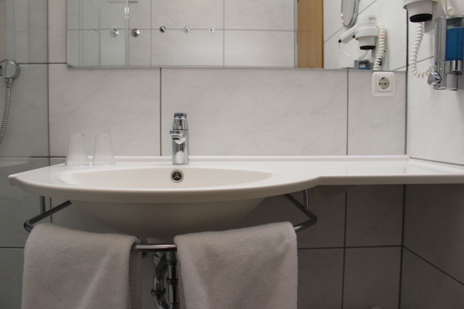 A bathroom with a white sink, a mirror above it, and a towel rack with two towels.