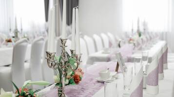 Una larga mesa de comedor con sillas blancas, un candelabro como centro de mesa y un mantel individual morado.