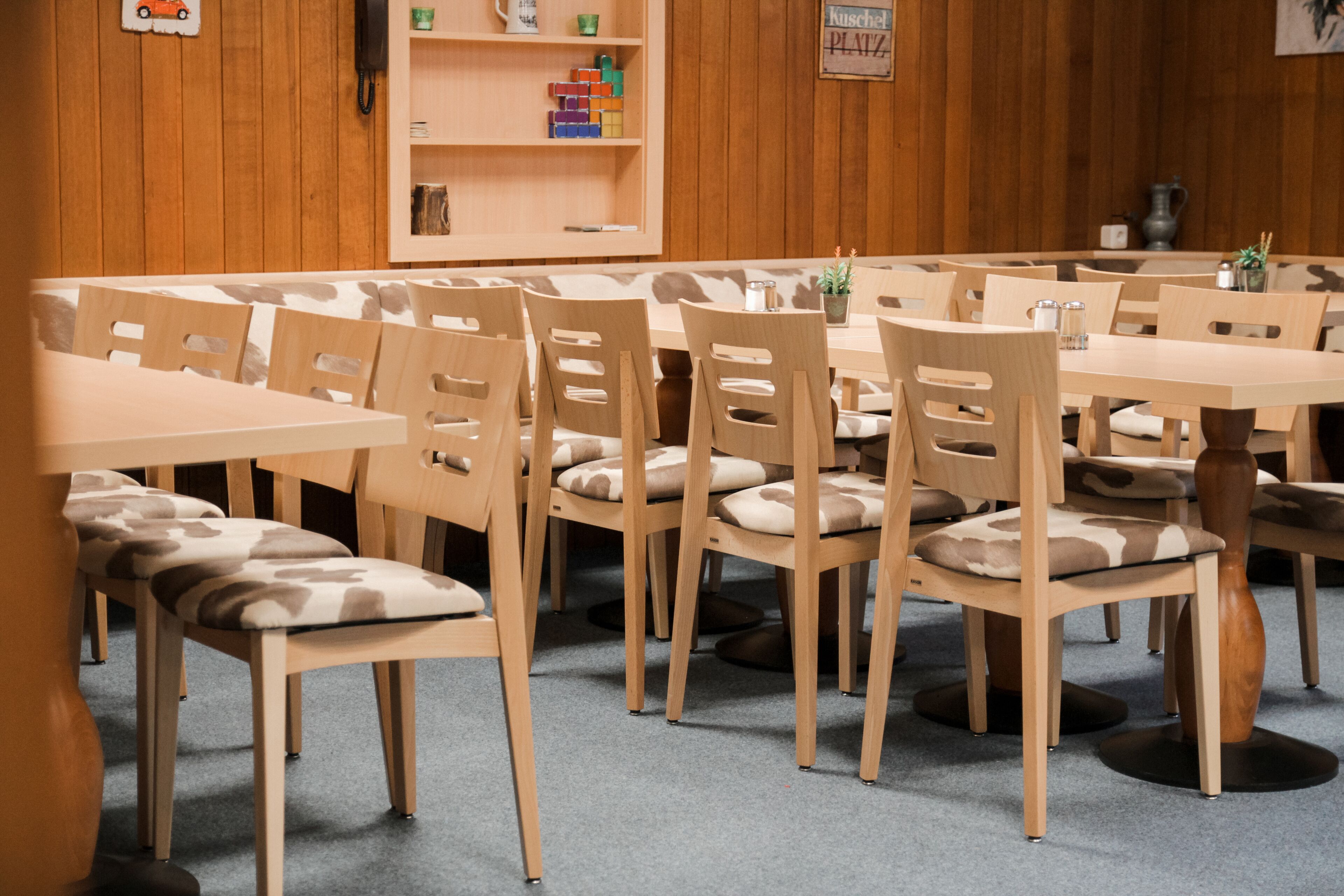 A dining area with multiple wooden tables and chairs, a bookshelf with toys, and a sign indicating a children's play area.