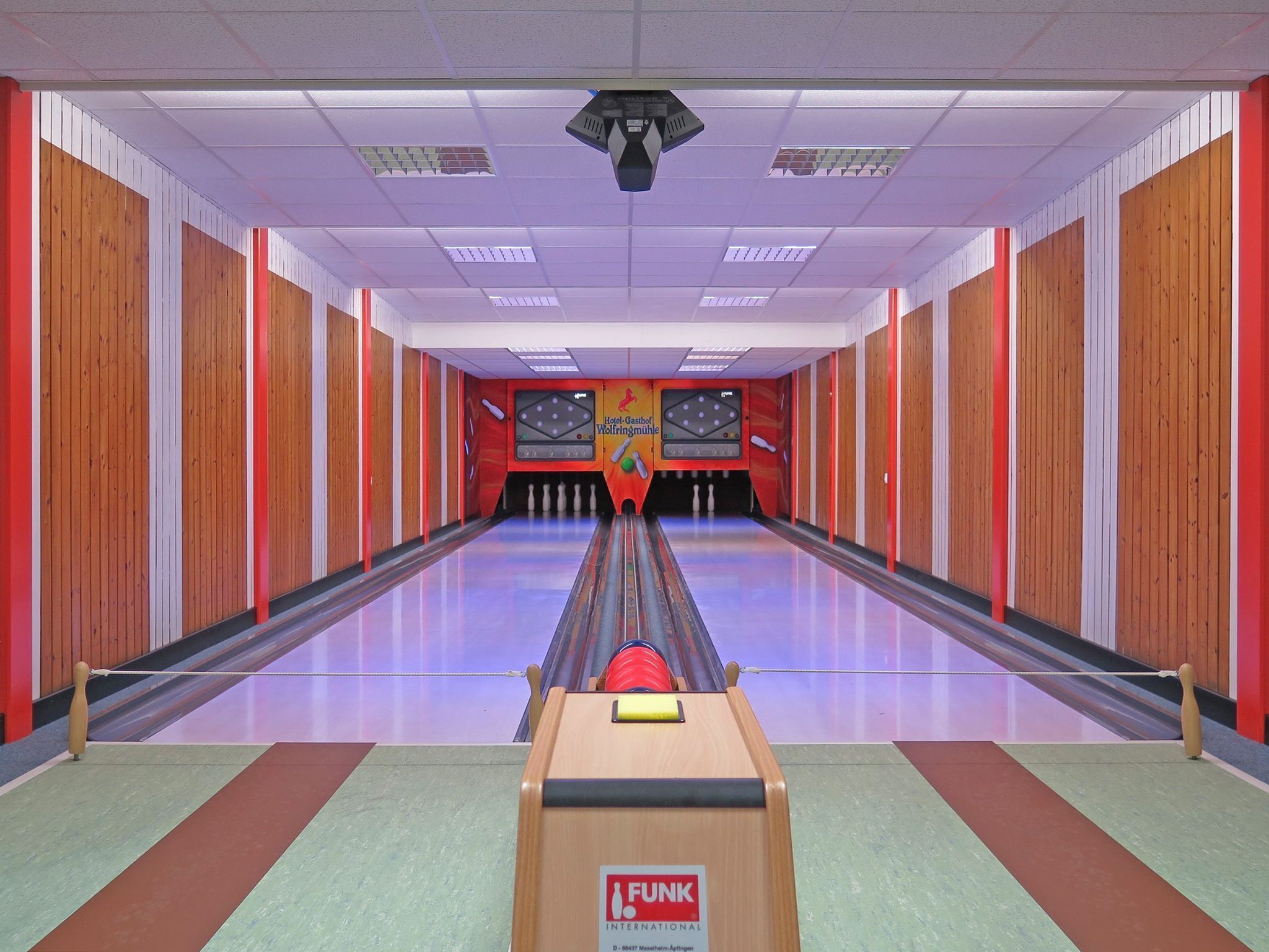 Une salle de bowling avec un plancher en bois, une piste de bowling et le logo de Funk International sur la machine à remettre les quilles.