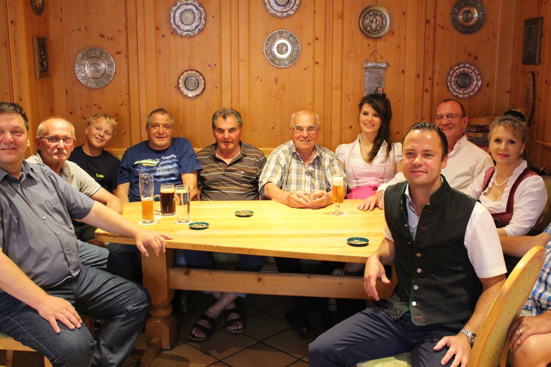 A group of people seated around a wooden table in a room with wooden paneling and decorative plates on the walls.