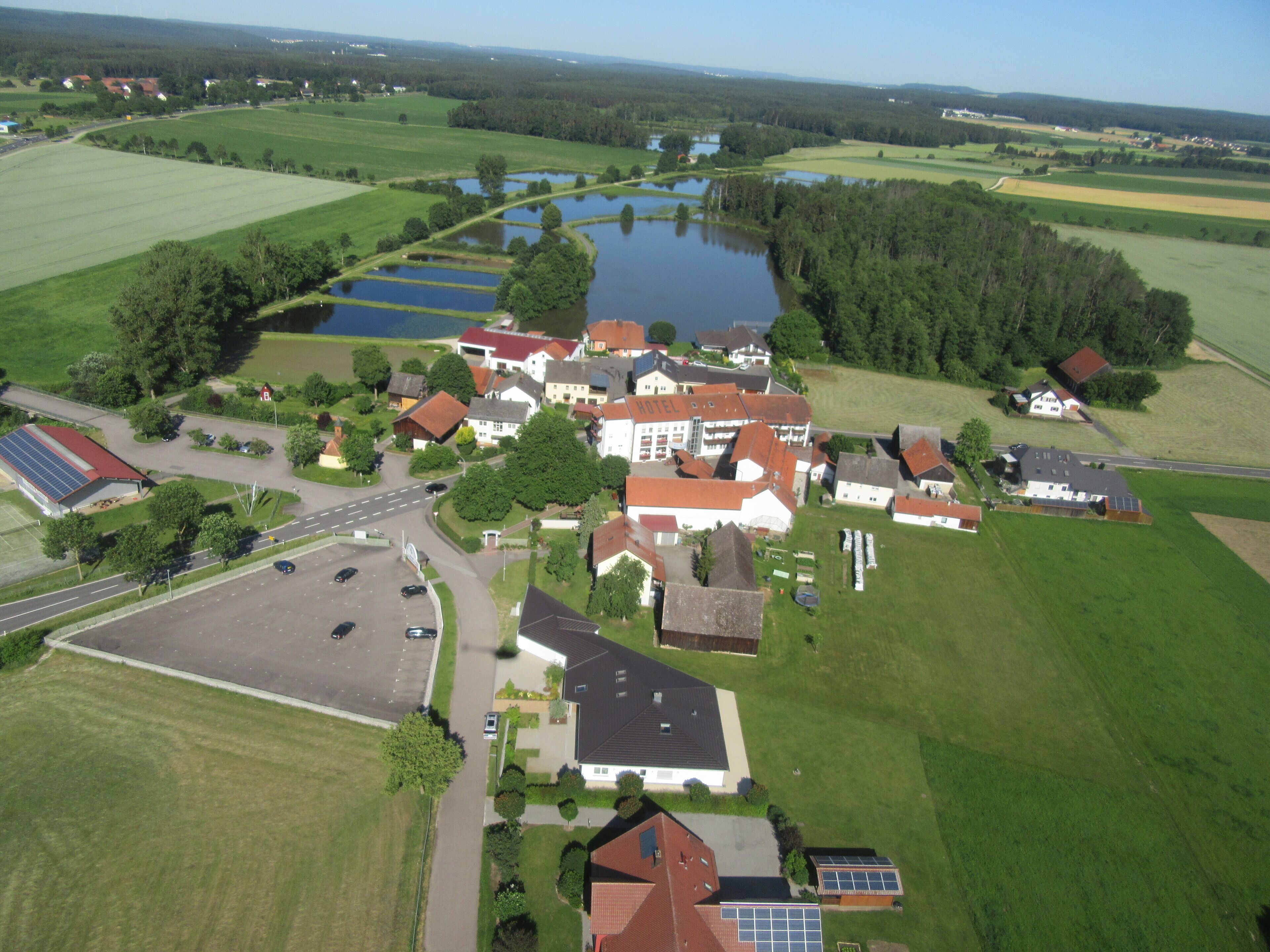 An aerial view of a rural area with a hotel, surrounded by fields, a lake, and a road.