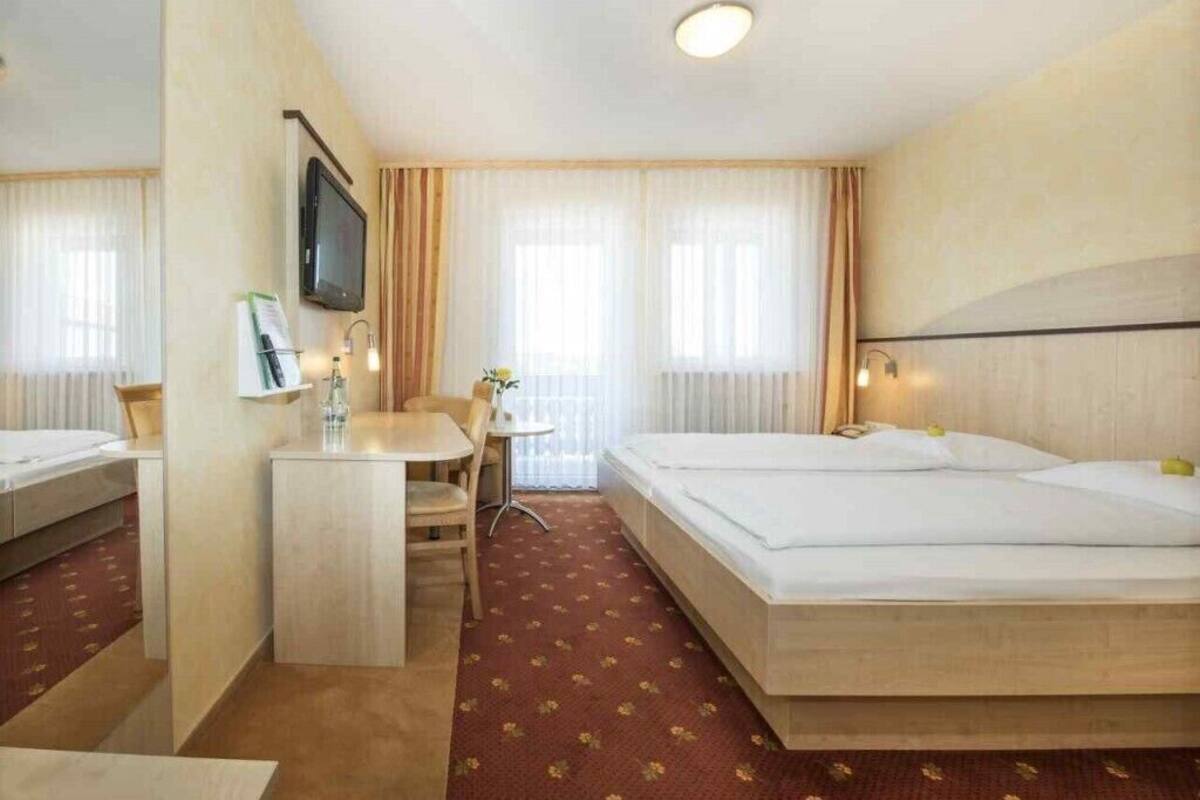 Une chambre d’hôtel avec un lit, un bureau, une chaise, une télévision et une fenêtre avec des rideaux.