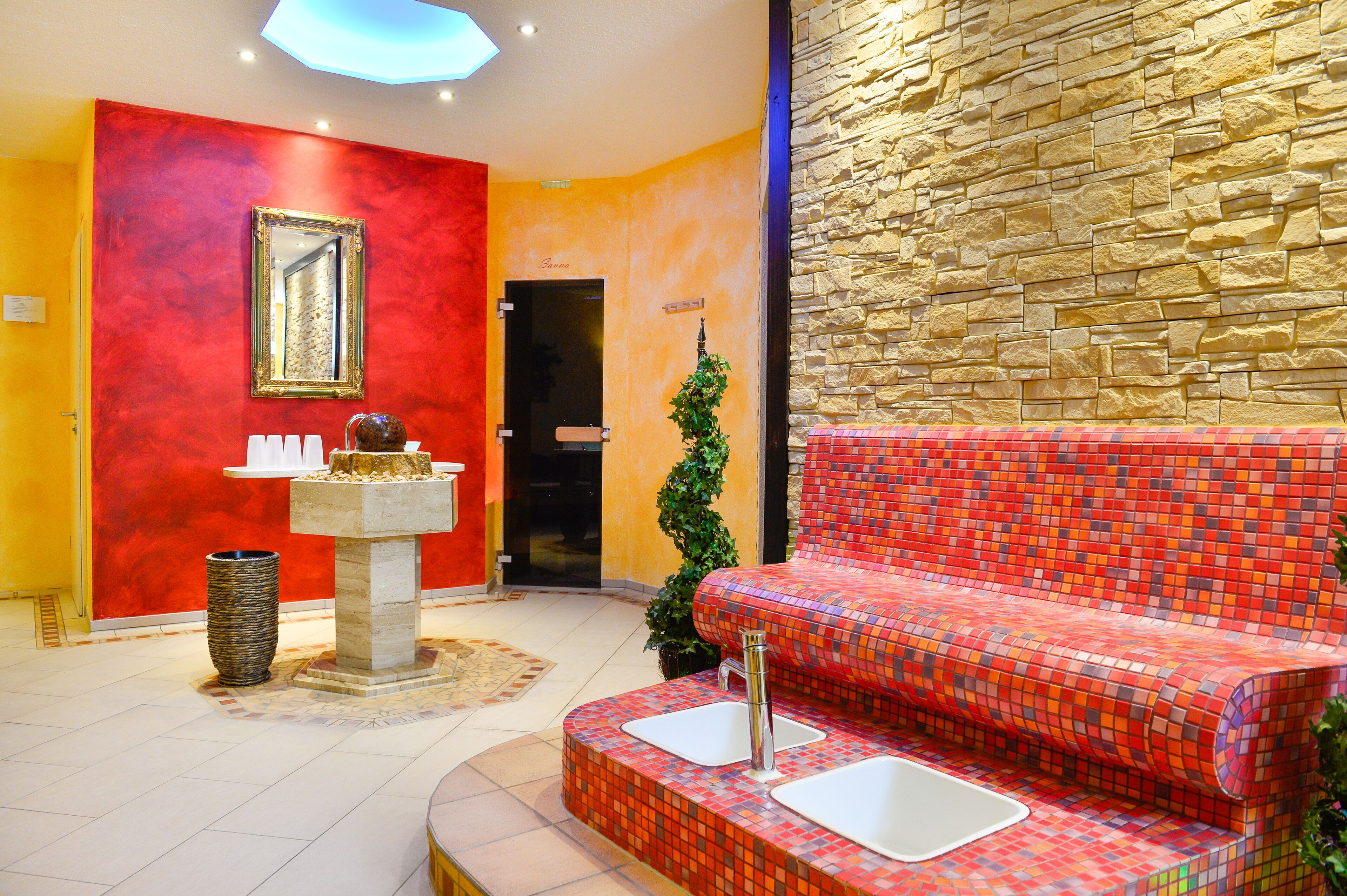 Un vestíbulo con pared roja y amarilla, pared de piedra, sofá con lavamanos integrados, espejo y cubo de basura.