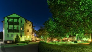 Hotel met een groen verlichte gevel, een zichtbaar balkon en een goed onderhouden tuin met terras.