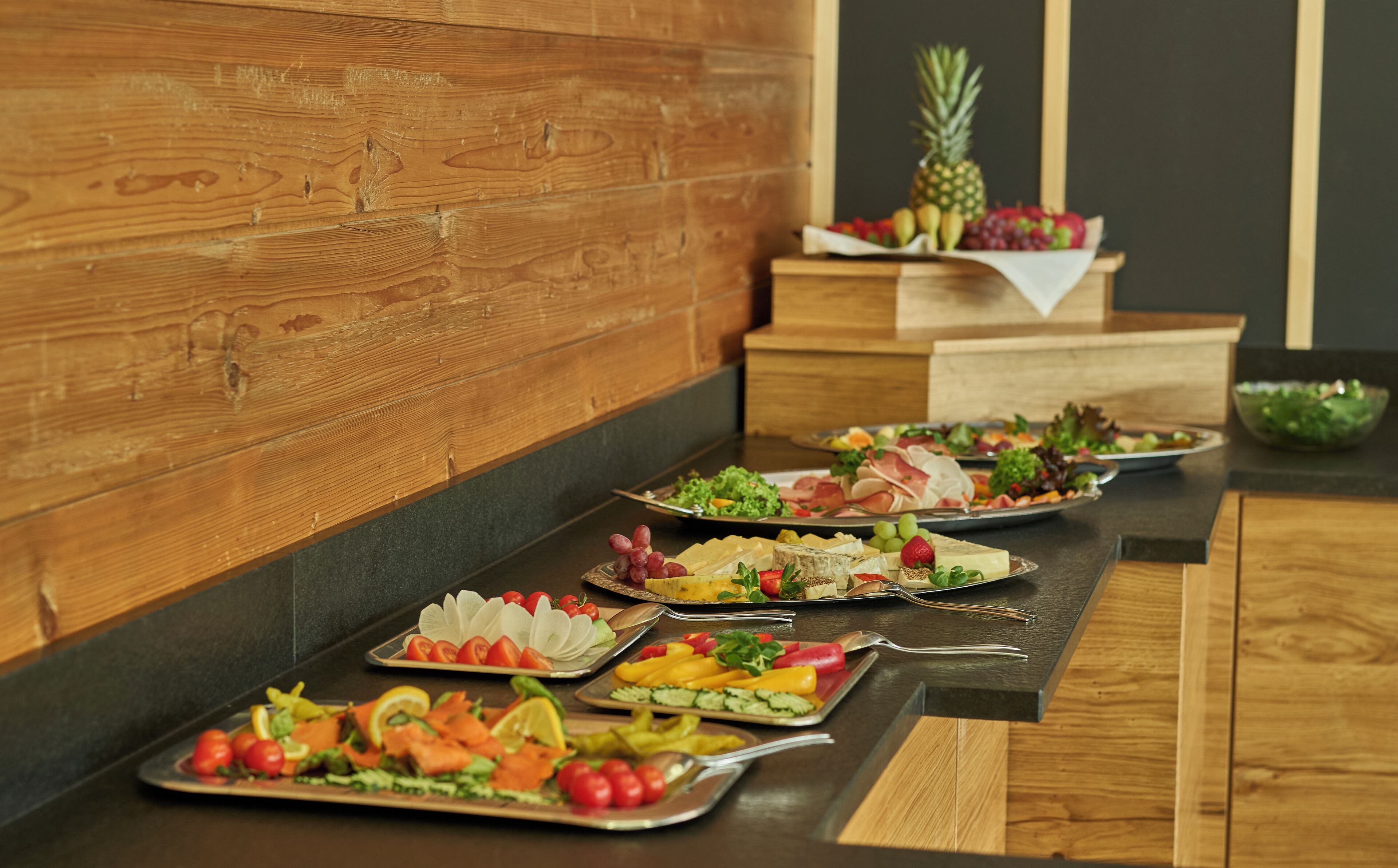 A buffet table with various food items including salads, fruits, and cheeses.